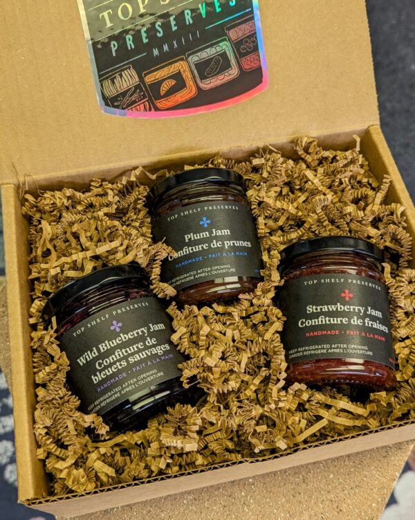 three jars of jam in a kraft paper box with crinkle paper and a holographic sticker that says Top Shelf Preserves